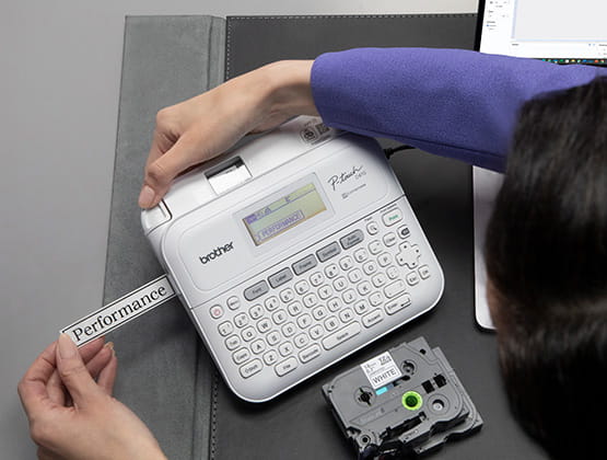 Person printing on P-touch PT-D410 with visible label tape cartridge on black desk
