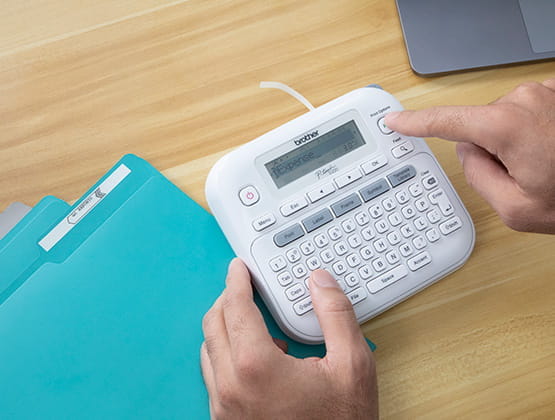 Person typing on Ptouch PT-D220 label maker on desk with teal file folders.