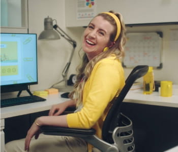 Yelena in yellow sitting at desk in front of computer