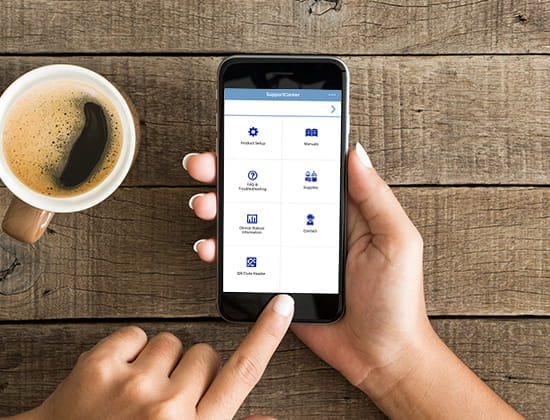Person holding mobile device in their hands which are resting on wood table with cup of coffee adjacent